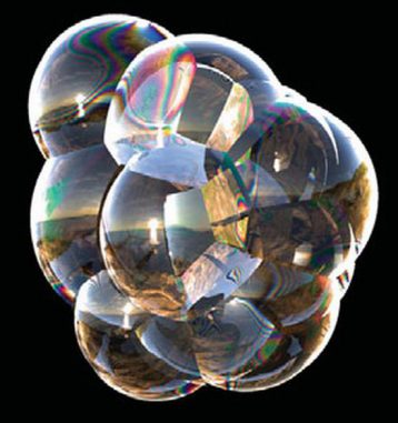 Eine Ansammlung von Seifenblasen mit Wechselwirkungen, die Regenbogenfarbtöne hervorbringen, ähnlich wie ein Ölfleck auf Asphalt. Die Blasen reflektieren einen Strand bei Sonnenuntergang. (UC Berkeley)