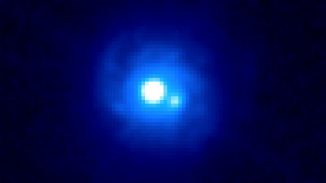 Hubble-Aufnahme der Gravitationslinse B0218+357. Sie zeigt zwei helle Quellen, die nur etwa eine Drittel Winkelsekunde voneinander getrennt sind. Jede Quelle ist ein Bild des Blazars im Hintergrund. Die Spiralarme gehören zu der beugenden Galaxie und sind ebenfalls sichtbar. (NASA / ESA and the Hubble Legacy Archive)
