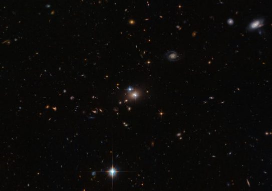 Der Zwillingsquasar QSO 0957+561 leuchtet hell in der Bildmitte. Das Doppelbild entsteht durch eine sogenannte Gravitationslinse, bei der ein näher liegendes Objekt (hier eine Galaxie und ein Galaxienhaufen) das Licht eines entfernten Objekts (hier der Quasar) beugt. (ESA / Hubble & NASA)