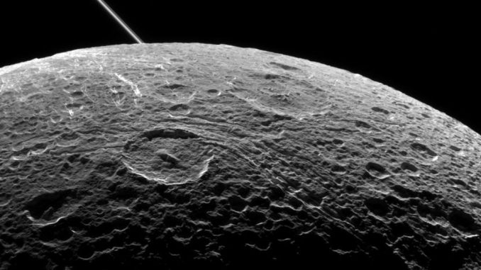 Der Saturnmond Dione während eines Vorbeiflugs der Raumsonde Cassini am 16. Juni 2015. Die diagonale Linie oben links sind die Saturnringe, aufgenommen aus einiger Entfernung. (NASA / JPL-Caltech / Space Science Institute)