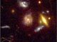Hubble-Aufnahme von fernen, hellen Radiogalaxien, deren Strahlung von einem sehr großen Galaxienhaufen im Vordergrund gebündelt wird. Die roten Konturen zeigen die Radioemissionen der Galaxien. (NASA HST, and van Weeren et al.)
