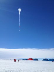 Ein weißer Ballon der BARREL-Mission schwebt in den antarktischen Himmel. Die Gebäude im Hintergrund gehören zur neuen Forschungsstation Halley VI, die in der Wintersaison 2012/2013 erstmals voll einsatzfähig ist. (NASA / R. Millan)