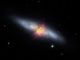 Kompositbild der Zigarrengalaxie M82. Das von SOFIA registrierte Magnetfeld (schwarze Linien) scheint den bipolaren Abströmungen (rot) zu folgen. Das Bild kombiniert sichtbares Licht (grau) und registriertes Wasserstoffgas (rot) des Kitt Peak Observatory mit nah- und mittelinfrarotem Sternlicht und Staub (gelb) von SOFIA und dem Weltraumteleskop Spitzer. (Credits: NASA / SOFIA / E. Lopez-Rodriguez; NASA / Spitzer / J. Moustakas et al.)