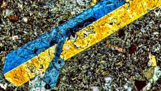 Ein Schnitt des Bohrkerns unter dem Mikroskop. Der blaugelbe Kristall ist Titanaugit, umgeben von verschiedenen Mineralen wie Feldspat, Phlogopit und Apatit. (Credits: Gazel Labs)