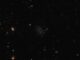 Ein schwarzes, größtenteils leeres Feld mit zerstreuten Sternen und Galaxien. In der Mitte liegt eine kleine, irreguläre Zwerggalaxie namens Donatiello II. (Credit: ESA /Hubble & NASA, B. Mutlu-Pakdil; Acknowledgement: G. Donatiello)