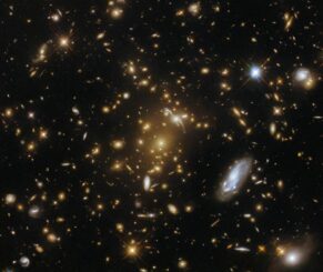 Der Galaxienhaufen eMACS J1823.1+7822, umgeben von zahlreichen Sternen und kleineren Galaxien. Der Galaxienhaufen dient als Gravitationslinse für das Licht verschiedener Hintergrundgalaxien. (Credit: ESA / Hubble & NASA, H. Ebeling)